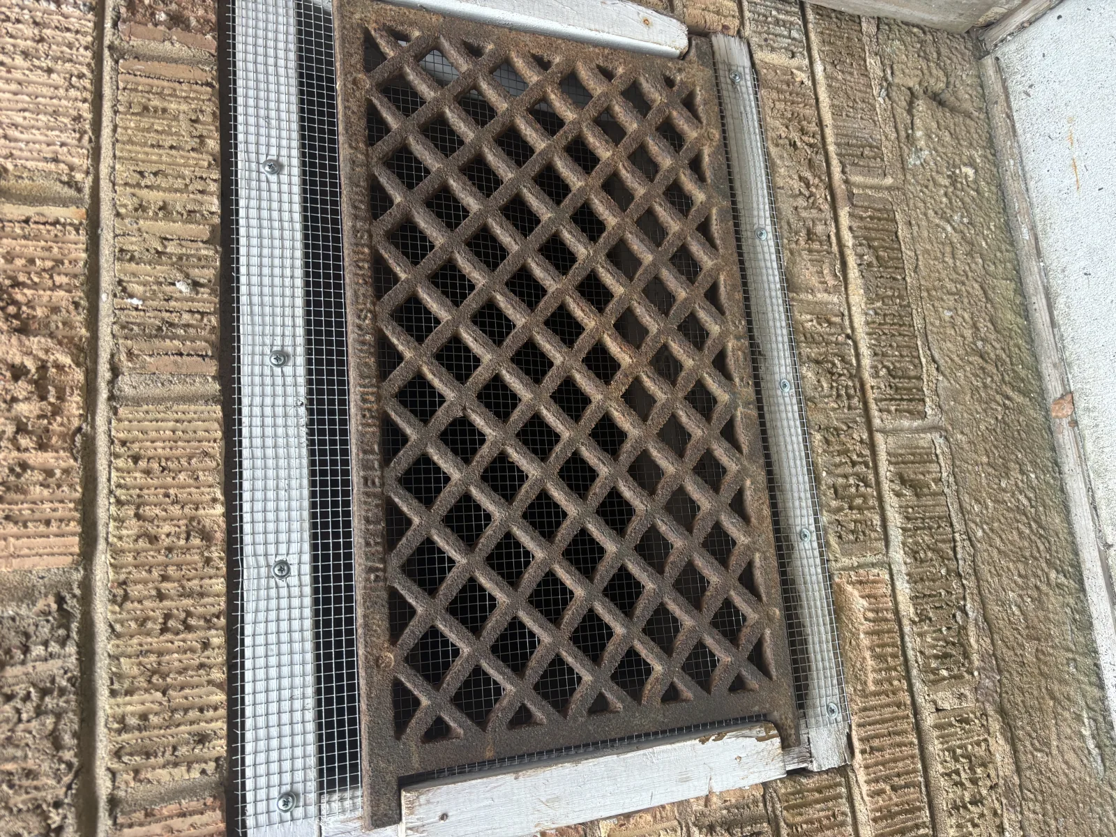 Foundation crawlspace vent with cast iron grate sealed with hardware cloth mesh