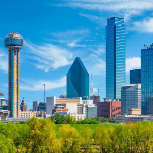 Spring foliage fills the foreground leading back to the skycrapers of Dallas skyline with clear blue sky above, Texas